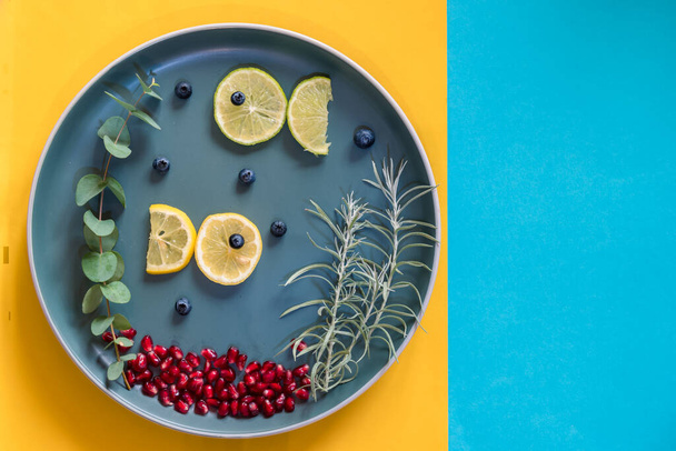 рыбы из ломтиков лимона, плавающие на тарелке с зелеными растениями, пространство для копирования изолировано на синем и желтом фоне - Фото, изображение