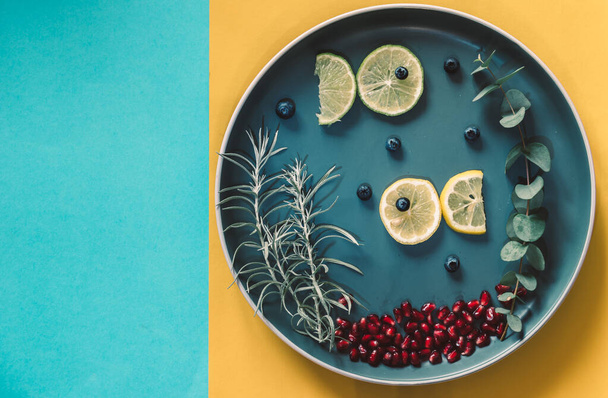 рыбы из ломтиков лимона, плавающие на тарелке с зелеными растениями, пространство для копирования изолировано на синем и желтом фоне - Фото, изображение