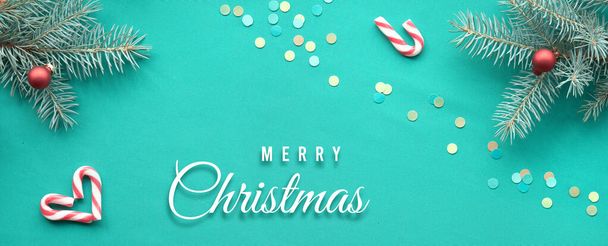 Christmas banner panoramic background. Text Merry Christmas on turquoise textile. Top view, flat lay on fir twigs with Xmas red decorations, hearts, candy canes. - Фото, зображення