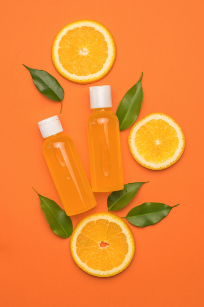 Dos botellas de jugo de naranja, hojas y trozos de naranja sobre un fondo naranja. El concepto de terapia con remedios naturales. Puesta plana. - Foto, imagen