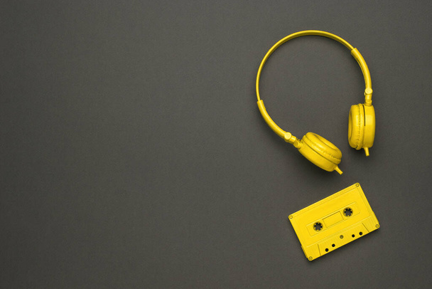 ein gelbes Tonbandgerät und gelbe Kopfhörer auf schwarzem Hintergrund. Farbtrend. Oldtimer-Geräte zum Musikhören. flache Lage. - Foto, Bild