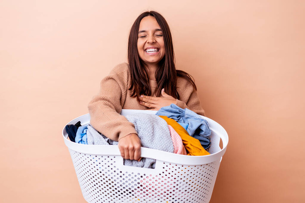Young mixed race woman holding a laundry isolated laughs out loudly keeping hand on chest. - Photo, Image