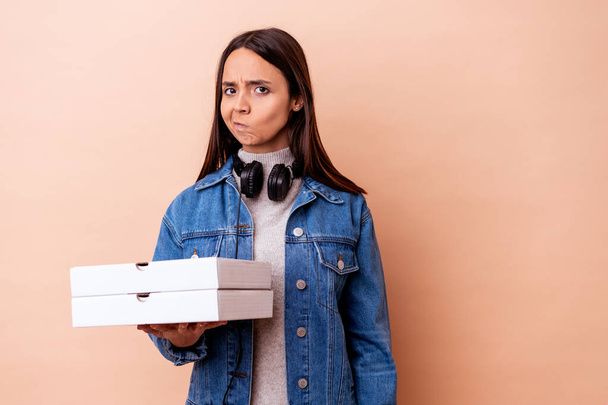 Young mixed race woman holding a pizza isolated confused, feels doubtful and unsure. - Foto, immagini