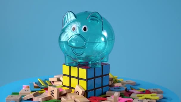 Sininen säästöpossu Rubikin kuution päällä. Rahatalouden ja tiedustelun käsitteet - Materiaali, video