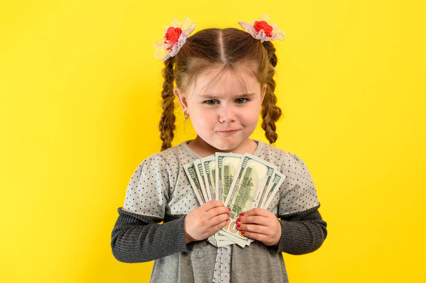 Kinder und finanzielle Verantwortung, kleines Mädchen auf gelbem Hintergrund mit Dollars in den Händen, finanzielle Alphabetisierung bei einem Kind. neu - Foto, Bild