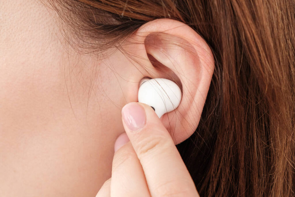 Woman inserts wireless headphone in the ear.  - Φωτογραφία, εικόνα