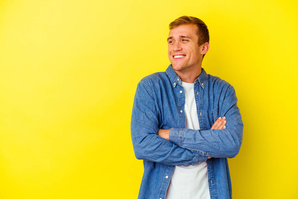 Young caucasian man isolated on yellow background smiling confident with crossed arms. - Photo, Image