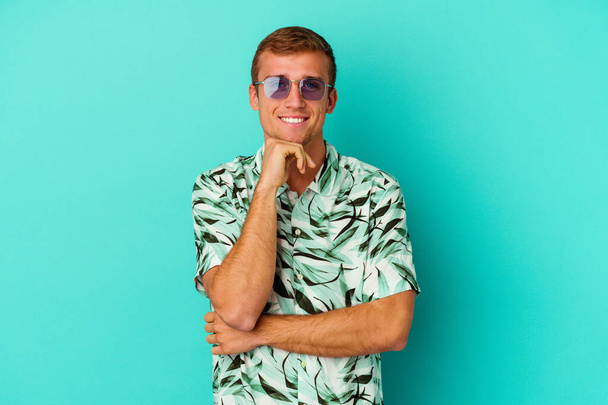 Jovem caucasiano vestindo uma roupa de verão isolado no fundo azul sorrindo feliz e confiante, tocando queixo com a mão. - Foto, Imagem