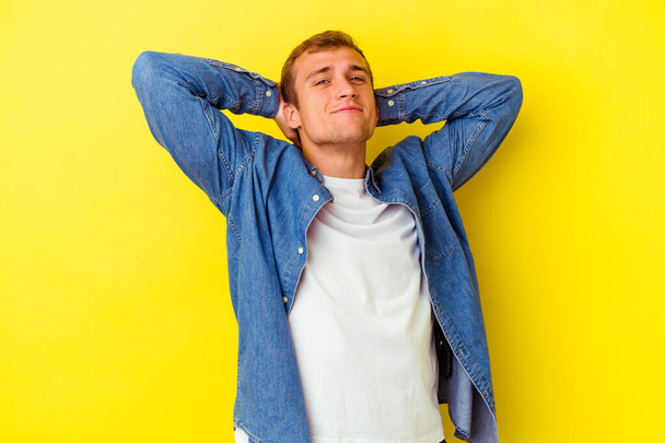 Young caucasian man isolated on yellow background feeling confident, with hands behind the head. - Photo, Image