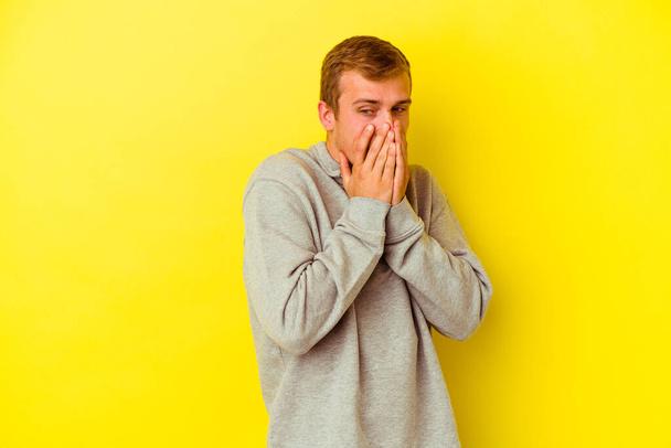 Jonge blanke man geïsoleerd op gele achtergrond lachen over iets, bedekken mond met handen. - Foto, afbeelding