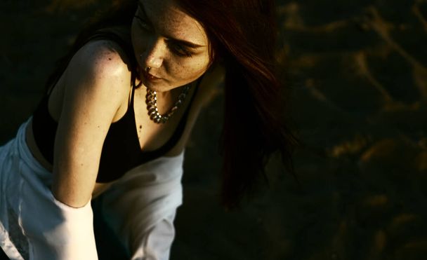 redhaired sensual girl in a white shirt thinking and sitting  on the sand - Foto, Imagen