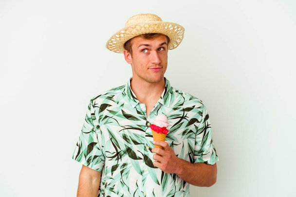 Joven hombre caucásico vistiendo una ropa de verano y sosteniendo un helado aislado sobre fondo blanco soñando con alcanzar metas y propósitos - Foto, imagen