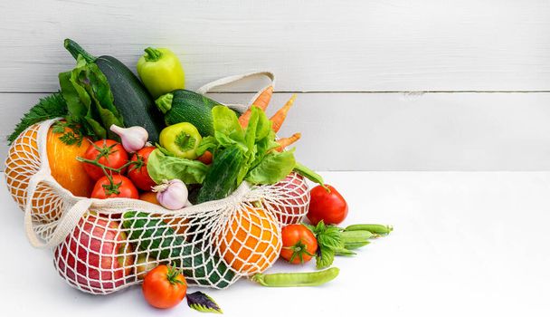 白い木製のテーブルの上に有機エコ野菜とメッシュショッピングバッグ。環境への配慮とプラスチック概念の拒絶 - 写真・画像