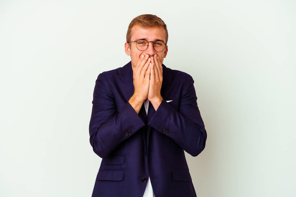 Νεαρός καυκάσιος άνδρας απομονωμένος σε λευκό φόντο γελώντας για κάτι, καλύπτοντας το στόμα με τα χέρια. - Φωτογραφία, εικόνα