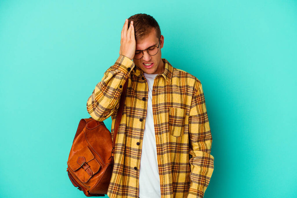Young caucasian student man isolated on blue background forgetting something, slapping forehead with palm and closing eyes. - Photo, Image