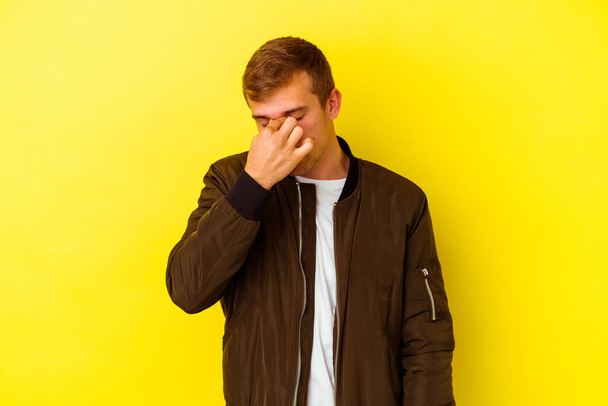 Young caucasian man isolated on yellow background having a head ache, touching front of the face. - Фото, изображение