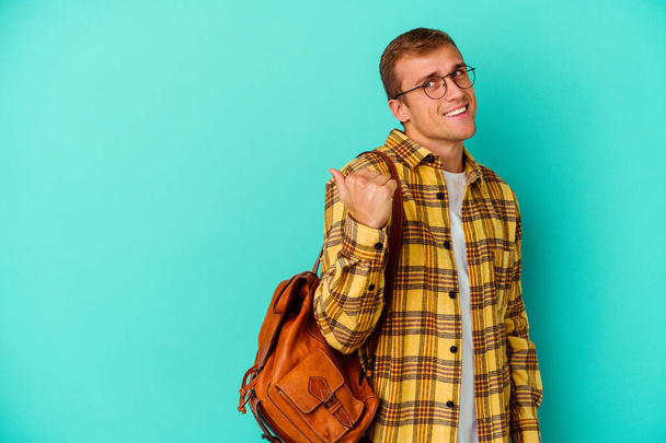 Jovem estudante caucasiano isolado em pontos de fundo azul com o dedo polegar de distância, rindo e despreocupado. - Foto, Imagem
