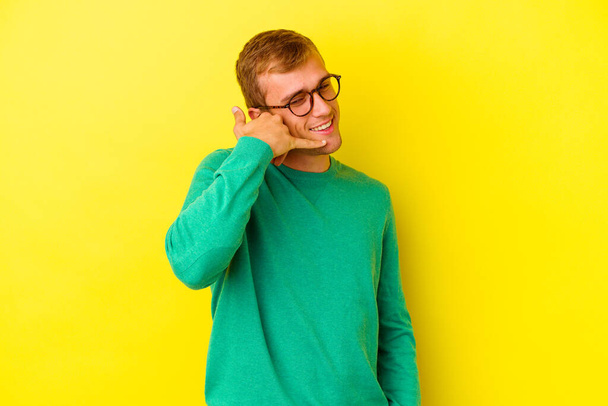 Young caucasian man isolated on yellow background showing a mobile phone call gesture with fingers. - Фото, зображення
