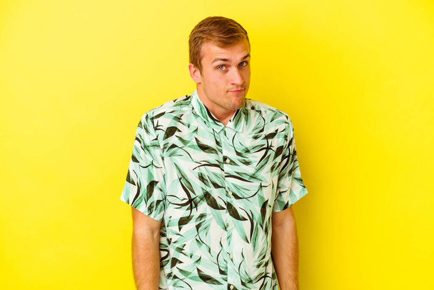 Young caucasian man isolated on yellow background shrugs shoulders and open eyes confused. - Photo, Image