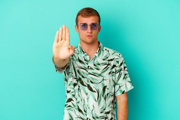 Junger kaukasischer Mann in Sommerkleidung isoliert auf blauem Hintergrund stehend mit ausgestreckter Hand, die Stoppzeichen zeigt und dich daran hindert. - Foto, Bild