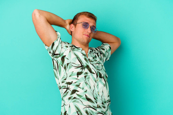 Fiatal fehér férfi visel nyári ruhát elszigetelt kék háttér nyújtózkodó karok, nyugodt helyzetben. - Fotó, kép