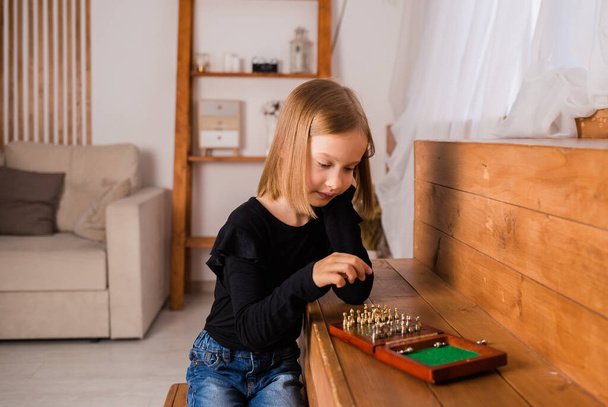 una niña rubia está jugando al ajedrez en la habitación. Intelectual juego - Foto, imagen