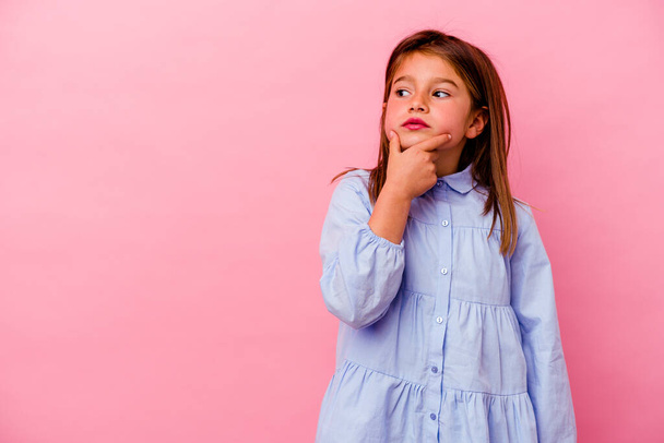 Little caucasian girl isolated on pink background  looking sideways with doubtful and skeptical expression. - Foto, Bild