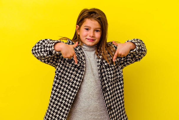 Маленька біла дівчинка ізольована на жовтому тлі вказує вниз пальцями, позитивне відчуття
. - Фото, зображення