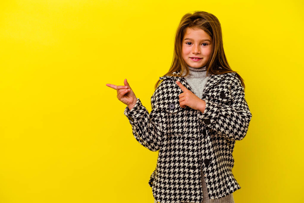 Маленька біла дівчинка ізольована на жовтому тлі шокована, вказуючи вказівниками пальців на простір копіювання
. - Фото, зображення