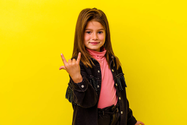 Little caucasian girl isolated on yellow background showing rock gesture with fingers - Photo, Image