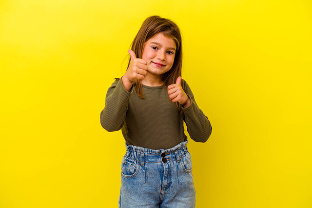 Kleines kaukasisches Mädchen auf gelbem Hintergrund, das beide Daumen nach oben hebt, lächelnd und selbstbewusst. - Foto, Bild