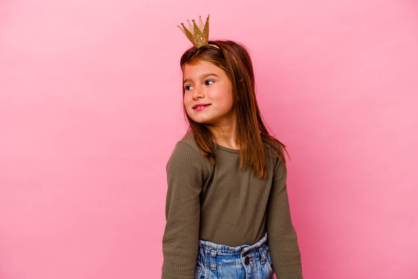 Pequeña princesa con corona aislada sobre fondo rosa soñando con lograr objetivos y propósitos - Foto, Imagen