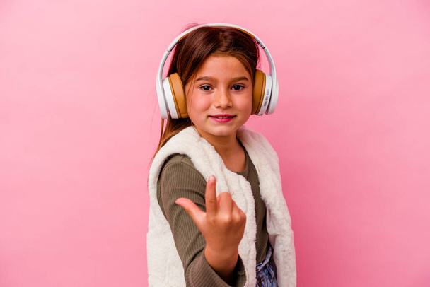 Pieni valkoihoinen tyttö kuuntelemassa musiikkia eristetty vaaleanpunainen tausta osoittaa sormella sinua ikään kuin kutsuva tulevat lähemmäksi. - Valokuva, kuva