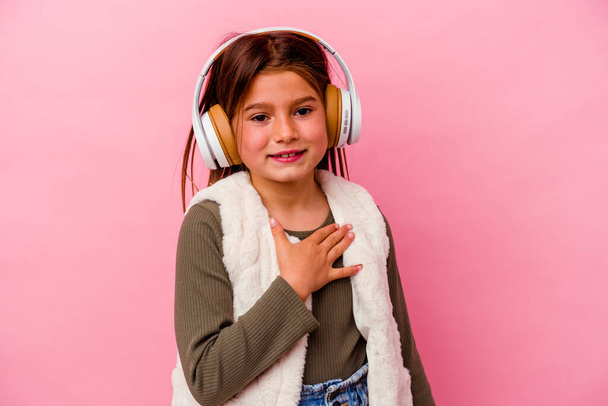Little caucasian girl listening music isolated on pink background laughs out loudly keeping hand on chest. - Foto, afbeelding