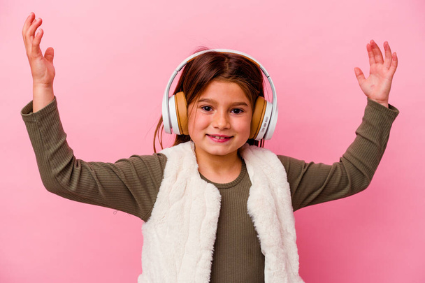 Menina caucasiana ouvindo música isolada no fundo rosa recebendo uma agradável surpresa, animado e levantando as mãos. - Foto, Imagem
