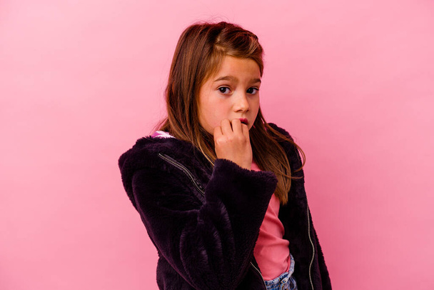Маленькая белая девочка, изолированная на розовом фоне, грызущая ногти, нервная и очень беспокойная.. - Фото, изображение