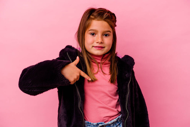 Pequeña chica caucásica aislada sobre fondo rosa persona señalando a mano a un espacio de copia de la camisa, orgulloso y confiado - Foto, imagen