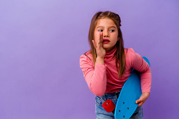 Μικρή καυκάσιος σκέιτερ κορίτσι απομονωμένο σε μπλε φόντο λέει ένα μυστικό ζεστό φρένο ειδήσεις και κοιτάζοντας στην άκρη - Φωτογραφία, εικόνα