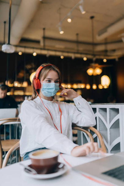 Una ragazza seduta in una caffetteria con le cuffie. Focolaio di coronavirus. - Foto, immagini