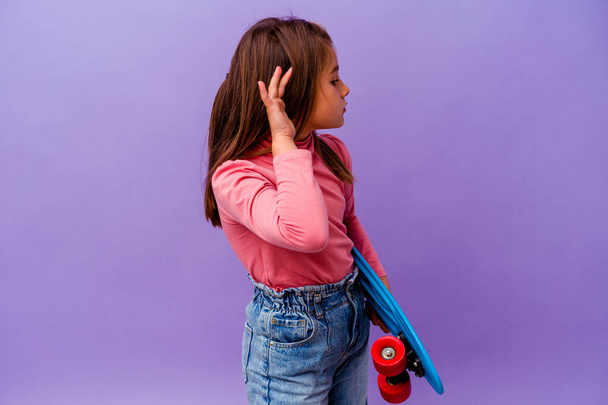 Piccolo pattinatore caucasico ragazza isolato su sfondo blu cercando di ascoltare un pettegolezzo. - Foto, immagini