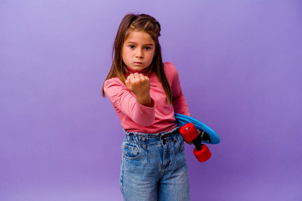 Маленькая белоснежная девочка на голубом фоне показывает кулак к камере, агрессивное выражение лица. - Фото, изображение