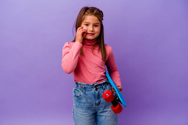 Little skater caucasian girl isolated on blue background with fingers on lips keeping a secret. - Photo, Image