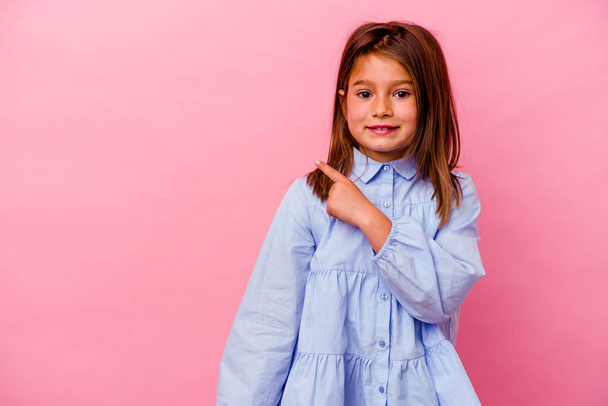 Little caucasian girl isolated on pink background  smiling and pointing aside, showing something at blank space. - Foto, immagini