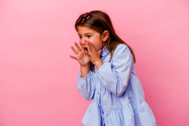 Little caucasian girl isolated on pink background  shouts loud, keeps eyes opened and hands tense. - Foto, imagen