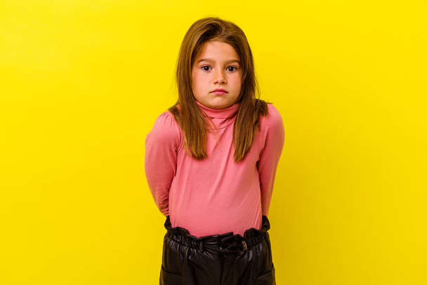 Kis kaukázusi lány elszigetelt sárga háttér garnélarák vállak és nyitott szemmel zavaros. - Fotó, kép
