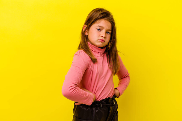 Petite fille caucasienne isolée sur fond jaune fronçant les sourcils dans le mécontentement, garde les bras croisés. - Photo, image