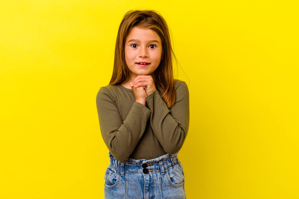 Kleines kaukasisches Mädchen auf gelbem Hintergrund, das um Glück betet, erstaunt ist und den Mund öffnet und nach vorne schaut. - Foto, Bild