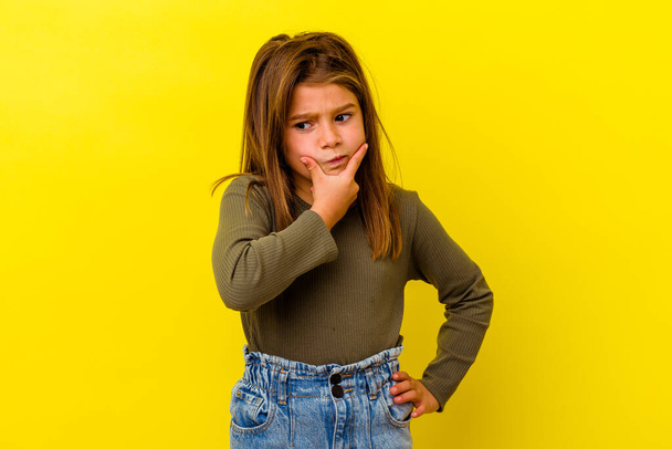 Little caucasian girl isolated on yellow background contemplating, planning a strategy, thinking about the way of a business. - Foto, imagen
