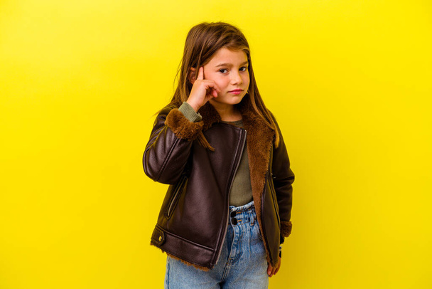 Petite fille caucasienne isolée sur fond jaune couvrant les oreilles avec les mains. - Photo, image