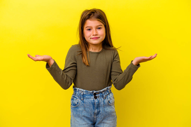Pequena menina caucasiana isolado no fundo amarelo faz escala com os braços, se sente feliz e confiante. - Foto, Imagem